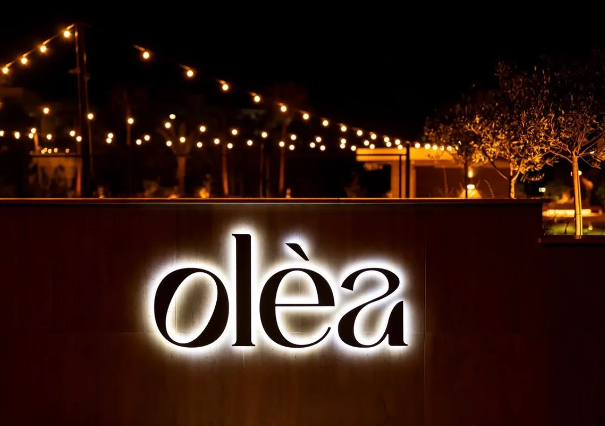 Η φωτισμένη επιγραφή του Κτήματος Olea το βράδυ, κάτω από τα λαμπιόνια